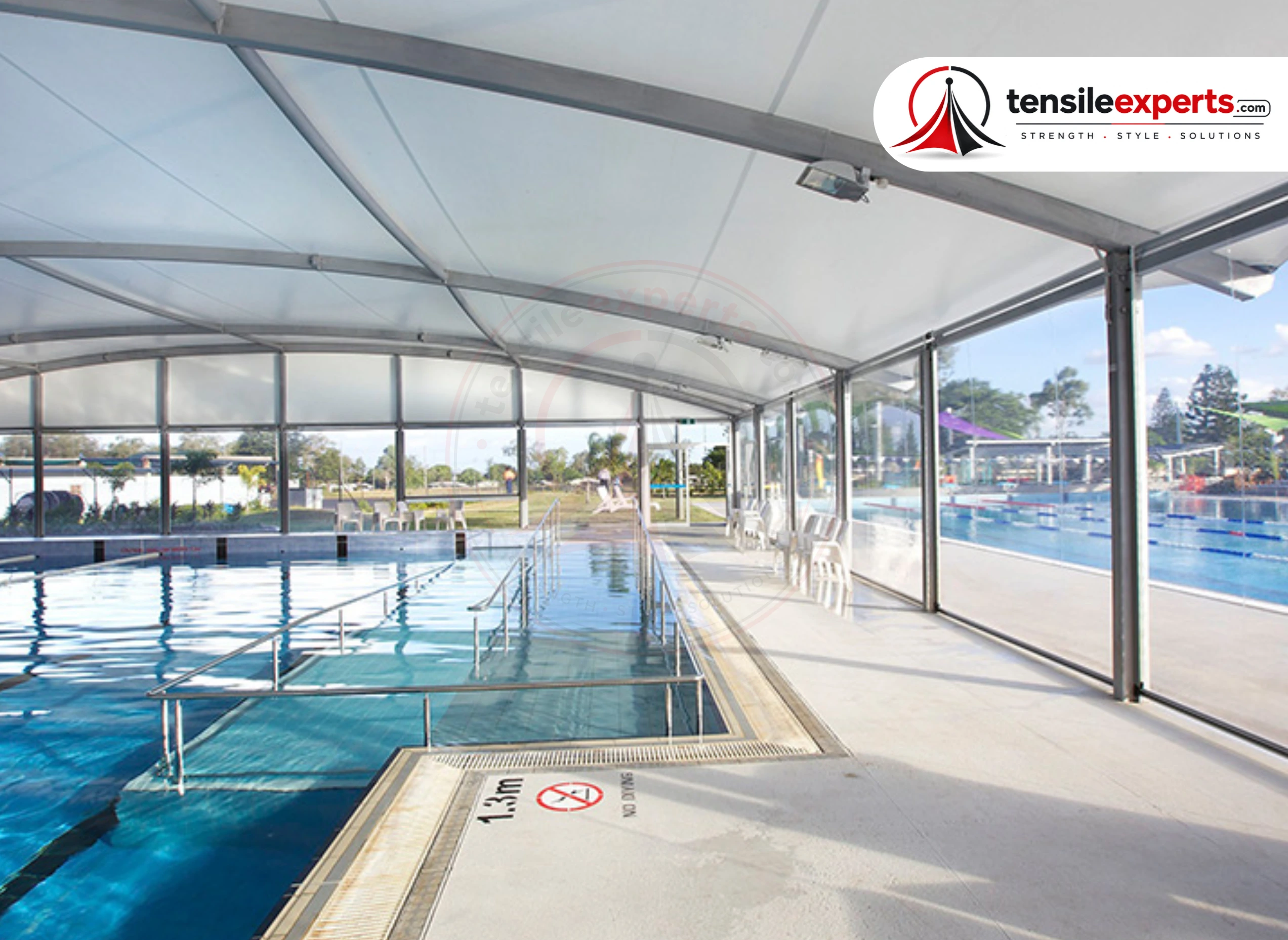 A fully-enclosed tensile pool structure — glass side panels with a curved fabric roof.
