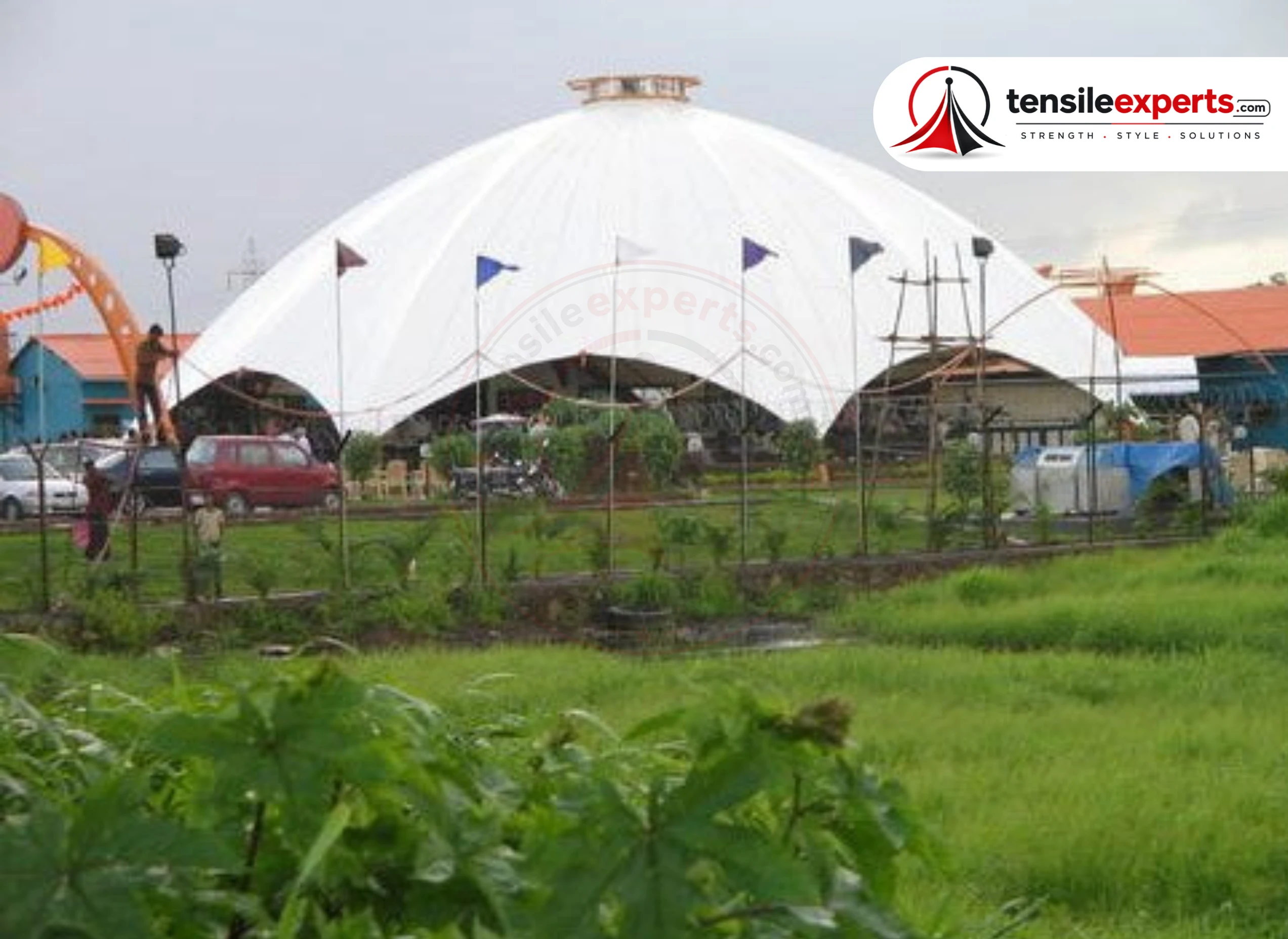 A tensile dome structure with flag-topped mast, flanked by connected barrel-vault sections.