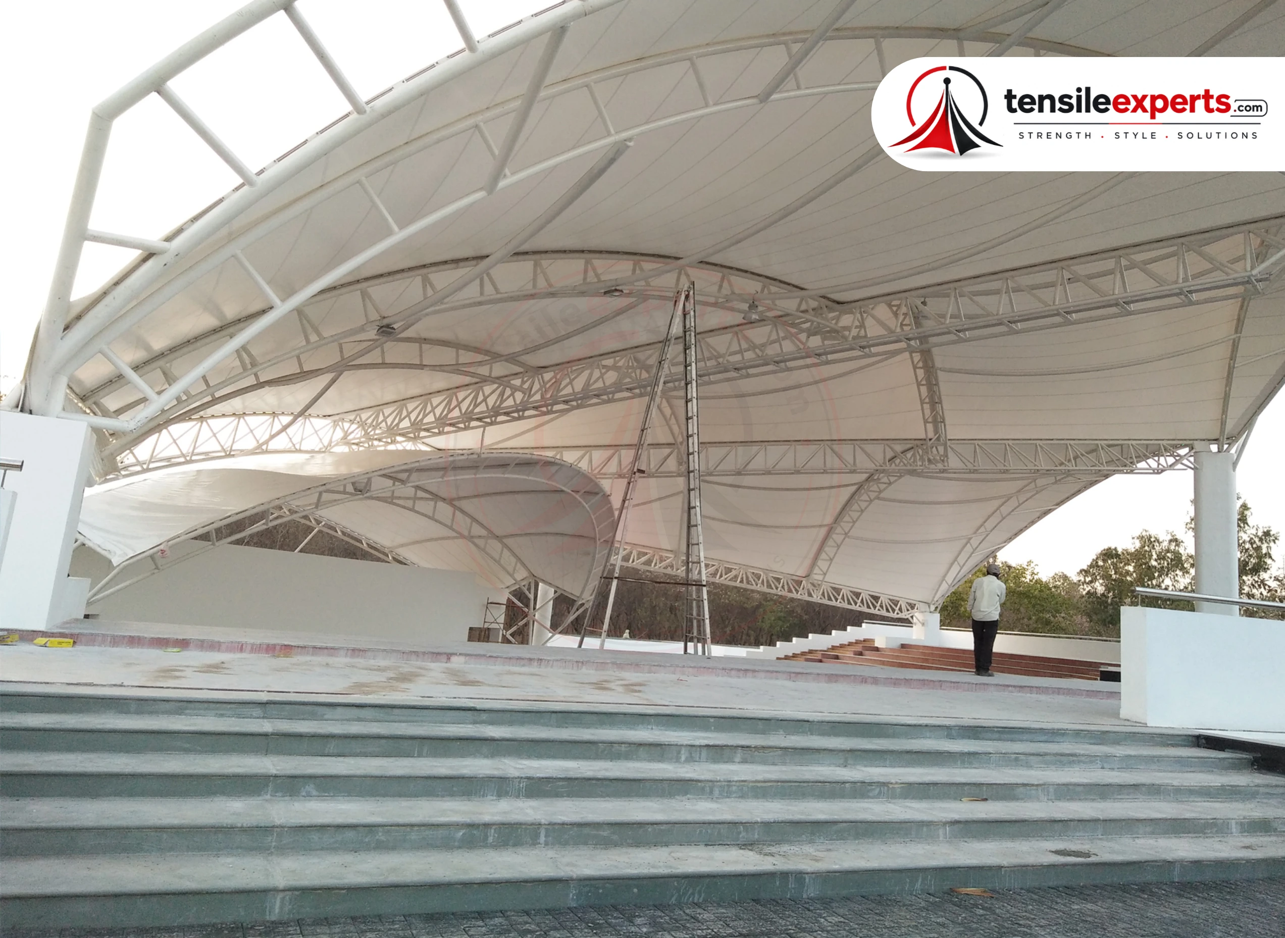 A tensile roof structure over an amphitheater-style gathering space — the same large-span principle applies to a corporate campus atrium or walkway.
