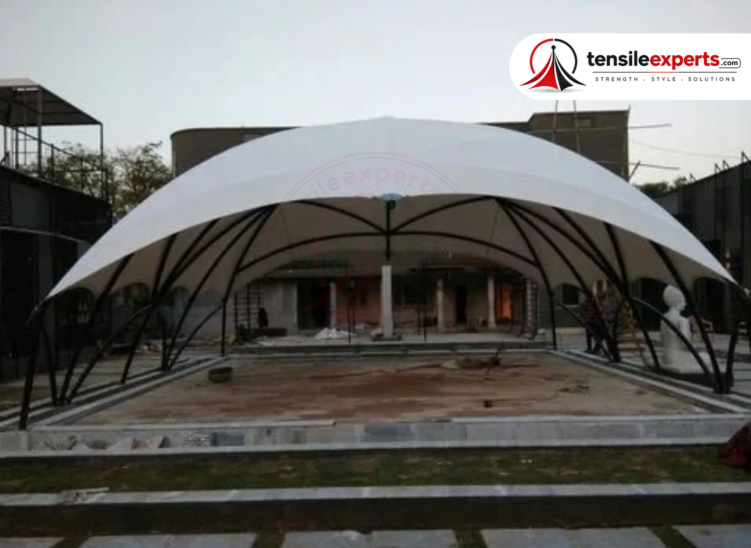 A tensile umbrella structure over a poolside seating spot — single-column, unobstructed underneath.