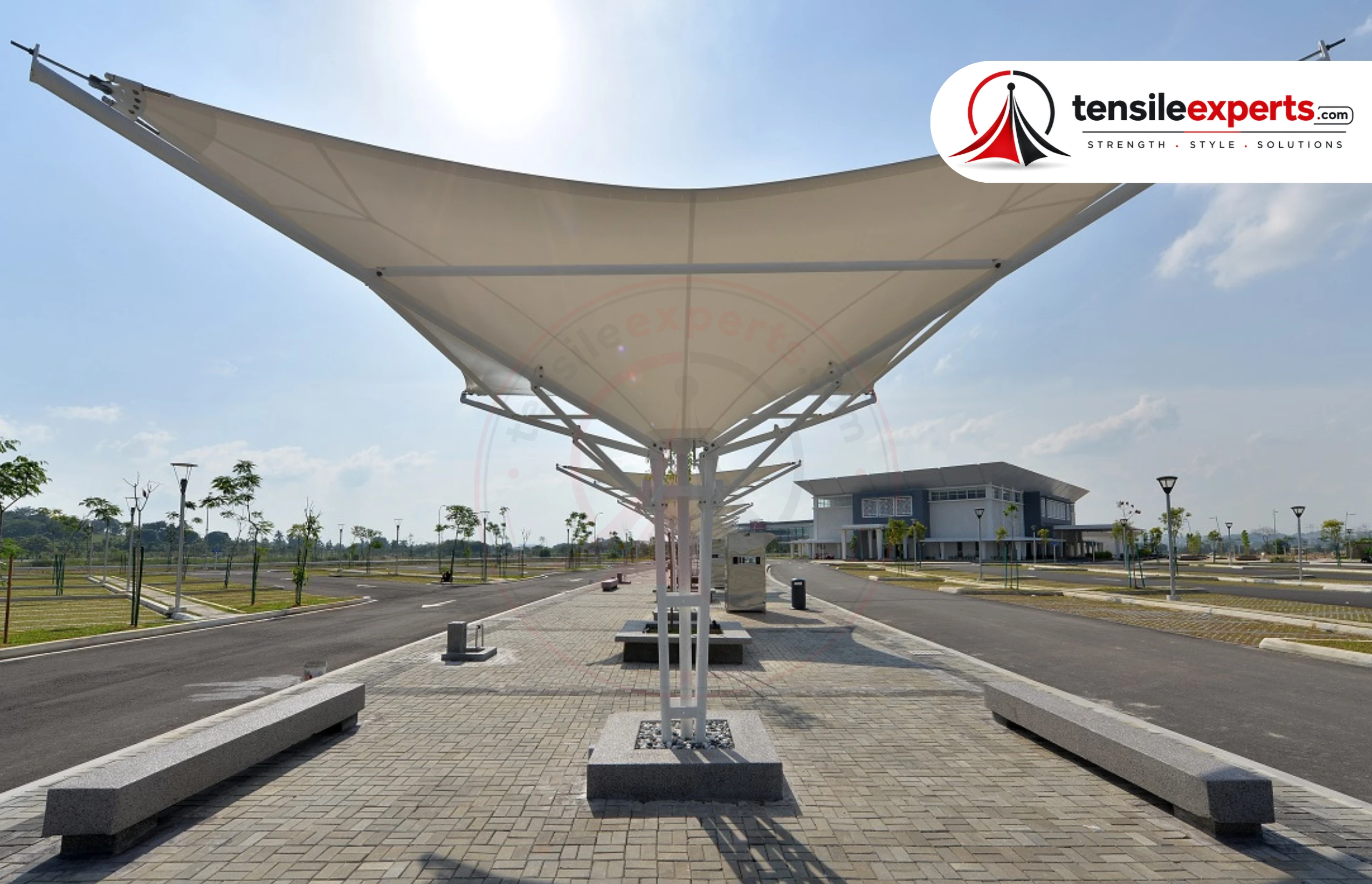 Slender sail-form tensile canopy at a campus walkway